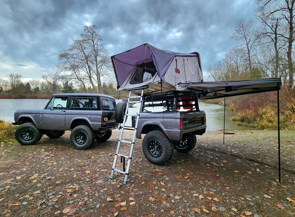 Bronco with camping trailer and tent parked along the riverbank